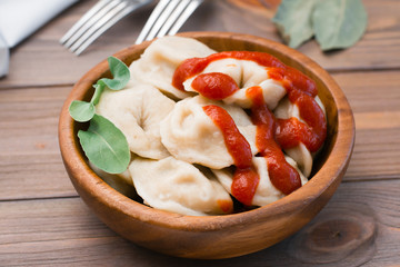 Cooked dumplings poured with ketchup with arugula leaves in a wooden bowl on the table