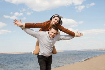 Happy man carrying his girlfriend on back like plane outdoors in sunny day