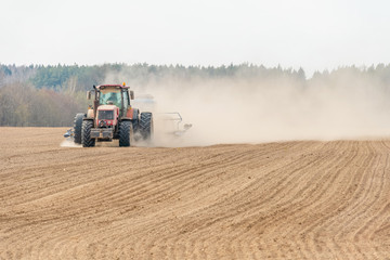 Naklejka premium Farmer in tractor preparing land with seedbed cultivator as part of pre seeding activities in early spring season of agricultural works at farmlands.