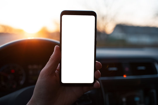 Man holds a smartphone with mockup in the car on sunset background