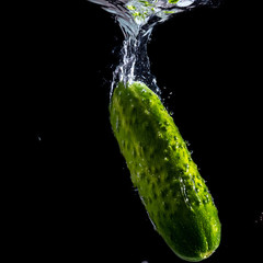 green juicy cucumber falls into the water with splashes
