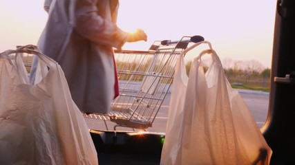 A woman stores packages from a store in a car trunk in a parking lot