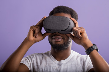 Handsome young African man in VR headset standing against purple background