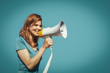 young smiling woman with megaphone isolated in blue background. communication and marketing concept.