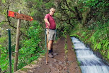 Senior tourist hiking at the 25 Fontes falls, a cascade waterfall at the end of a levada hike on the island Madeira