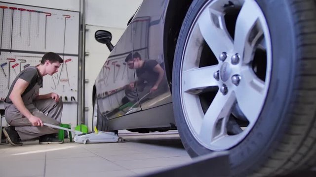 Male master raises the wheel of a car with a jack in order to repair it in a car repair shop. Tools, dent alignment, guy, repair, fix, professional. Dent Removal Tools