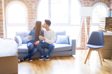 Young asian couple drinking a cup of coffee relaxing on the sofa at new home, smiling happy around cardboard boxes from moving