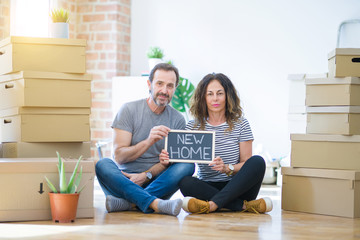 Fototapeta na wymiar Middle age senior couple sitting on the floor holding blackboard moving to a new home with a confident expression on smart face thinking serious