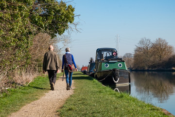 Couple walking along canal path beside narrow boat