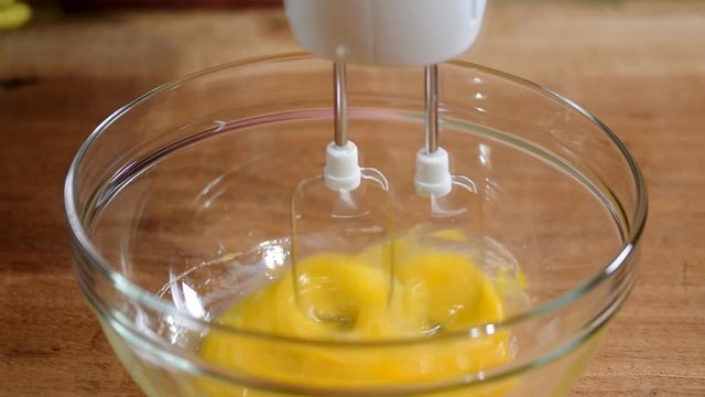 Woman hand beating eggs with brown sugar in bowl.