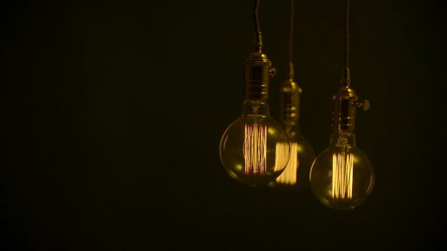 Three squirrel cage light bulbs on black background with copy space.