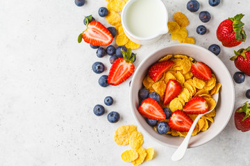 Cornflakes with strawberries and blueberries in a bowl on white background, top view.