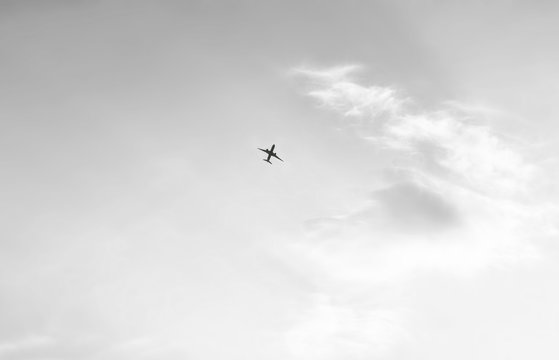 Minimalistic picture of the sky with light clouds and a flying plane in black and white format.