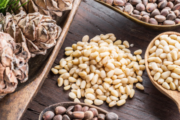 Pine nuts in the spoons and pine nut cone on the wooden table. Organic food.