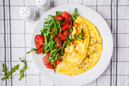 Classic omelet with cheese and tomatoes salad on white plate, top view.