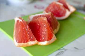 Slices of fresh, juicy grapefruit are on a green desk