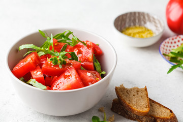 Tomatoes and arugula salad with sprouts and olive oil in gray bowl.