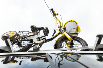 Fototapeta na wymiar Bicycle transport - a children's bicycle on the roof of a car against the sky in a special mount for cycling. The decision to transport large loads and travel by car