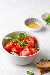 Tomatoes and arugula salad with sprouts and olive oil in gray bowl.