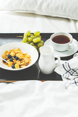 Breakfast in bed. Cornflakes with berries and milk, fruits and tea on black tray.