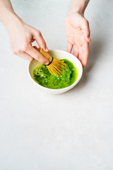 Woman in white prepare Japanese green Matcha tea by whipping it in a bowl with a bamboo Chasen whisk on a white background with copy space.