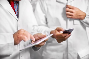 Employees confer stand in white coats using a tablet computer and telephone.