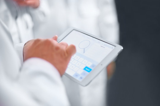Employees confer stand in white coats using a tablet computer and telephone.