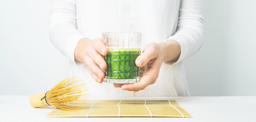 Close view of the glass with Japanese Matcha tea in womans hands on light background with copy space.  Long wide banner.