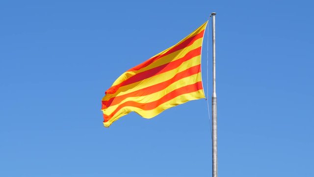 Catalonia flag wave in air against clear blue sky. Bright standard with four red horizontal bars on yellow field. Two times slow motion shot from 60 fps footage