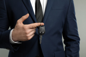 Young man holding car key on grey background, closeup
