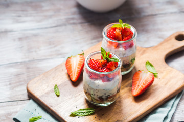 Yogurt granola parfait with strawberries and chia seeds. Healthy single portion breakfast served in glass cups on wooden board with green napkin. Natural wooden table background