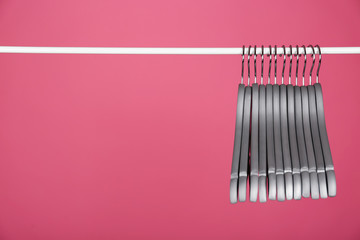 Empty clothes hangers on metal rail against color background. Space for text