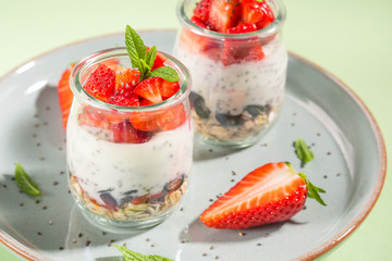 Yogurt granola parfait with strawberries and chia seeds. Healthy delicious dessert for breakfast. Mint green bright spring summer background