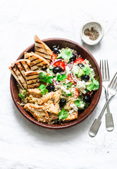 Mediterranean style lunch - couscous, cherry tomatoes, cucumbers, feta cheese, olives salad and lemon herbs roasted chicken breast on light background, top view