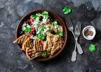 Mediterranean style lunch - couscous, cherry tomatoes, cucumbers, feta cheese, olives salad and lemon herbs roasted chicken breast on dark background, top view