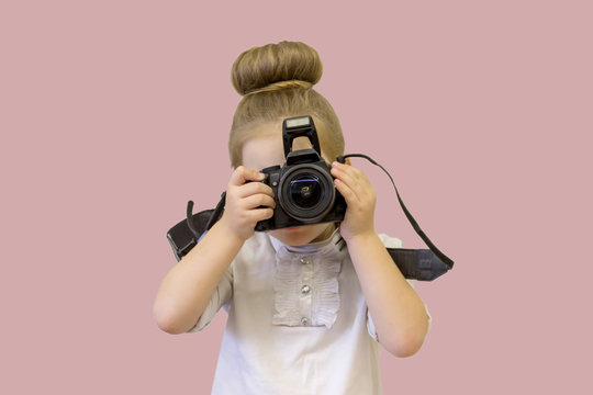 A little girl in business clothes holds a reflex camera in her hands in front of her face. The child wants to take a picture. The baby learns to take pictures and studies the complex technique