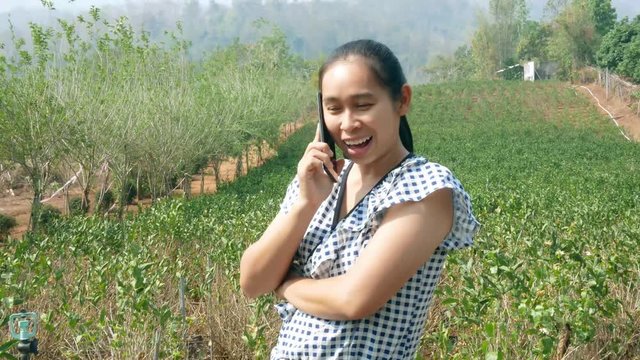 Asian young women talking by phone in the jasmine garden while sunshine to the face.