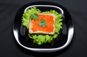 toast with red caviar and green salad on a black plate