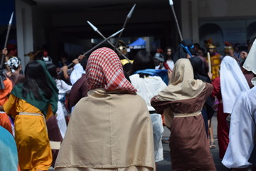 Mob of furious women persecuting Jesus Christ wearing scarf gaher on plaza cheering, ridicule, street drama, community celebrates Good Friday representing the events that led to his Crucifixion