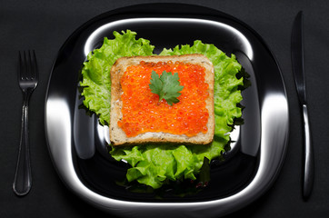 toast with red caviar and green salad on a black plate