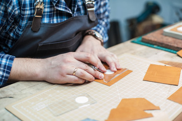 Man working with leather textile at a workshop. Concept of handmade craft production of leather goods.