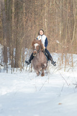 A young woman riding a brown horse in the forest
