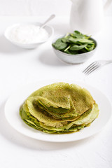 Spinach pancakes on white plate.  Stack of green crepes on white background.