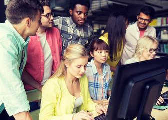 people, education, technology and school concept - group of happy smiling international students with computers at library in university