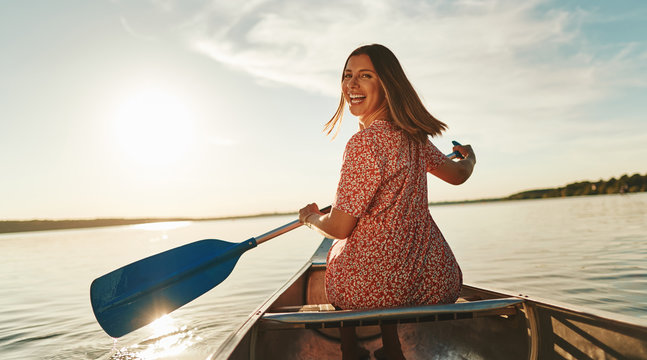 Smiling young woman paddling her canoe on a still lake