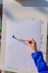 Artist's work place. A kid paints with blue gouache a picture. Open air workshop