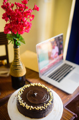 Dark chocolate cake with chocolate frosting and white chocolate chips with a computer in the background