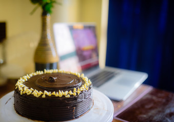 Dark chocolate cake with chocolate frosting and white chocolate chips with a computer in the background