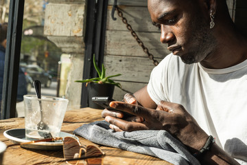 Young guy African American looking and typing with mobile phone. Concept of technology