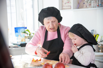 An old woman with a little girl in the kitchen. A little girl eats a piece of apple